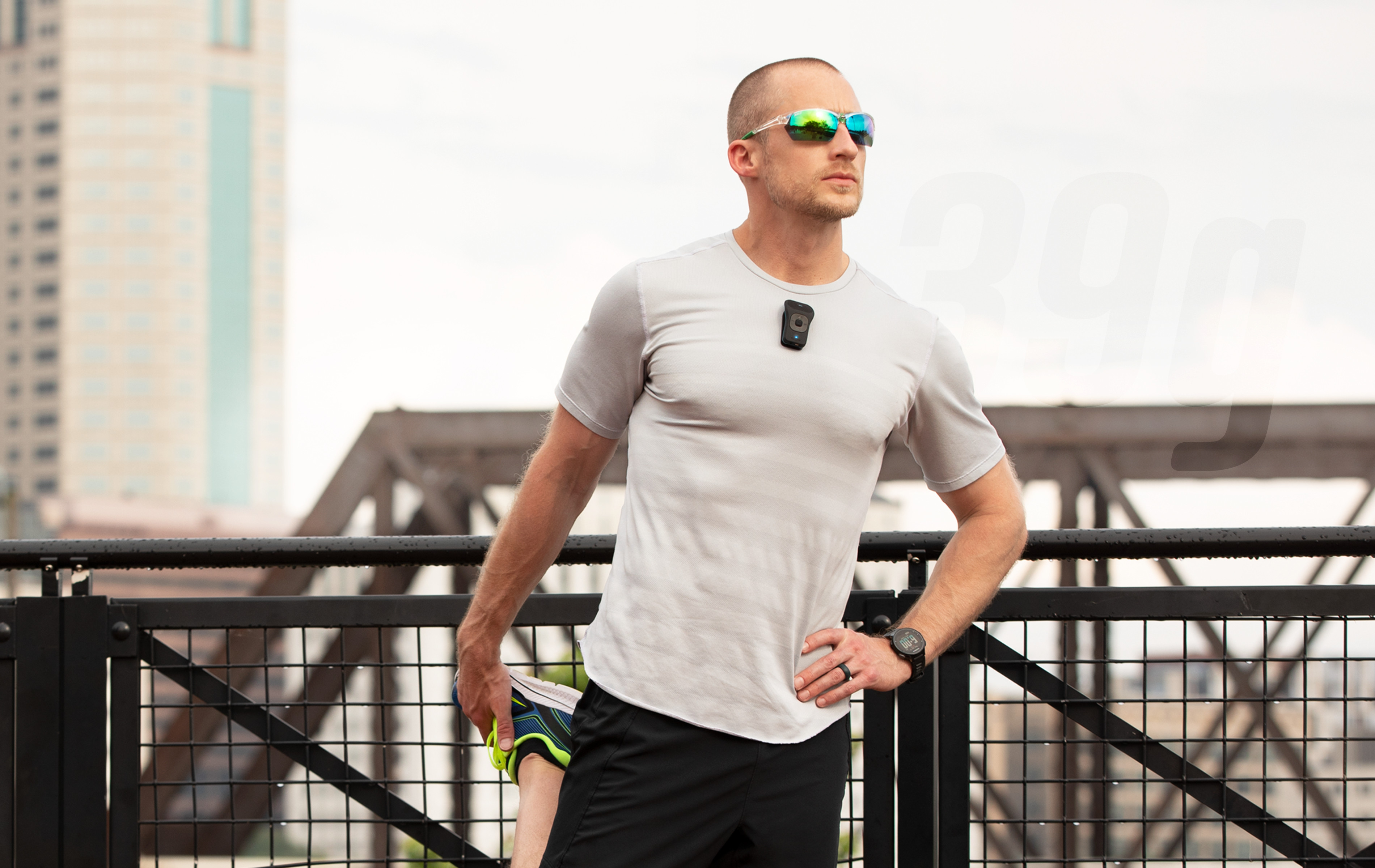 A man standing on a railing with a pair of sunglasses and a Bluetooth Speaker.