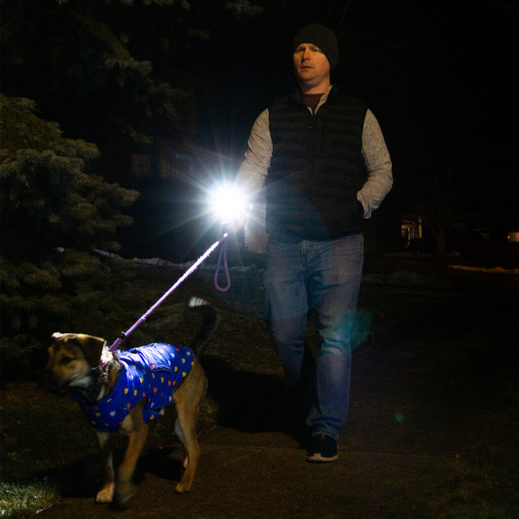 Man walking a dog using a Noxgear wrist strap with Tracer Lamp to illuminate his path. (Lamp not included in purchase of Wrist Strap)