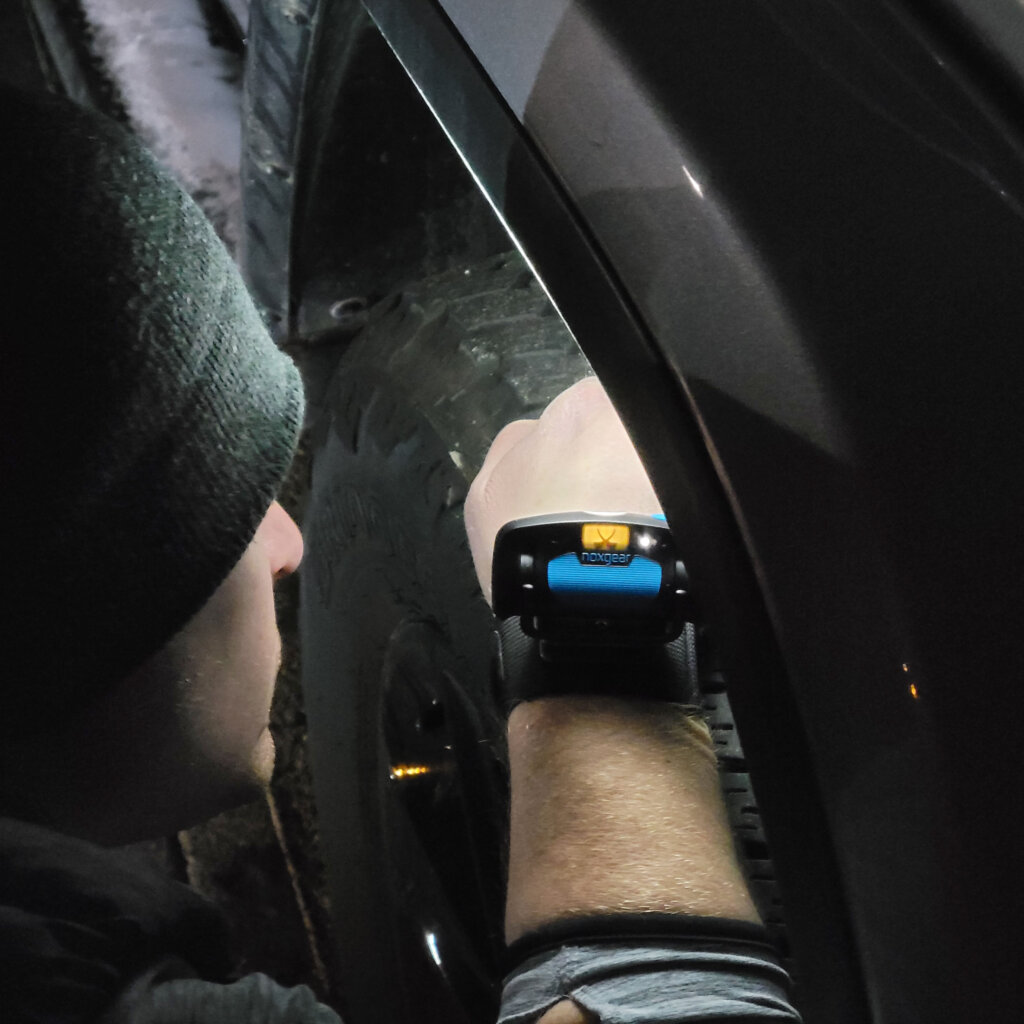 Man using the Noxgear Wrist Light to illuminate the wheel well of a car. (Lamp not included in purchase of Wrist Strap)
