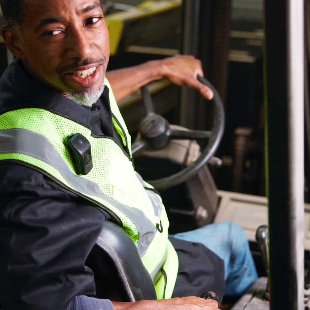Photo of a man driving a forklift in reverse while wearing a 39g on his construction vest.