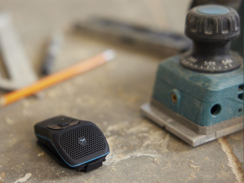 The Noxgear 39g sits on a wordworking table beside some tools and a pencil. This displays how small the speaker is for use on jobsites