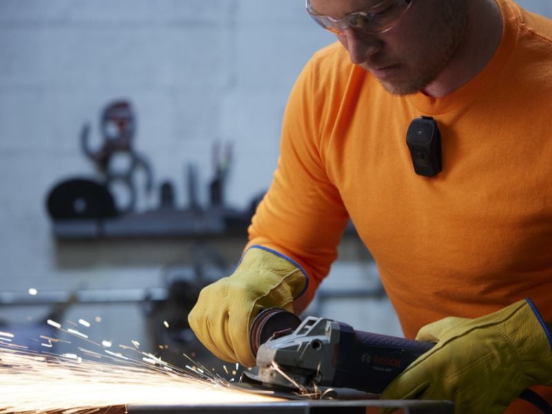 A man uses a metal grinder wearing safety glasses and a Noxgear 39g speaker.