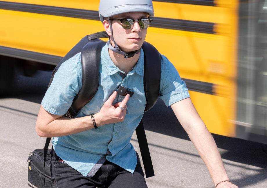 Man riding a bicycle wearing a 39g touching a button on the speaker.