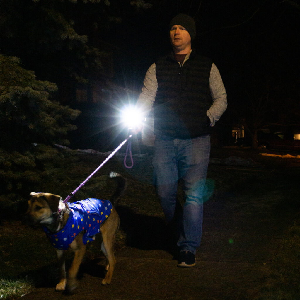 A person walking a dog. Beam from the Wrist Light illuminating the way in front of the dog.
