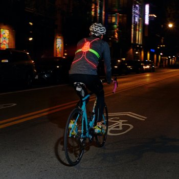 Man wearing a Tracer2 illuminated red, riding a blue road bike away from the camera.