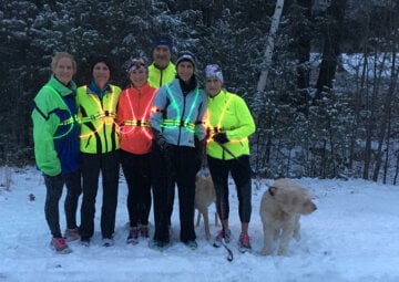 Six runners in noxgear pose in the snow with two distracted dogs